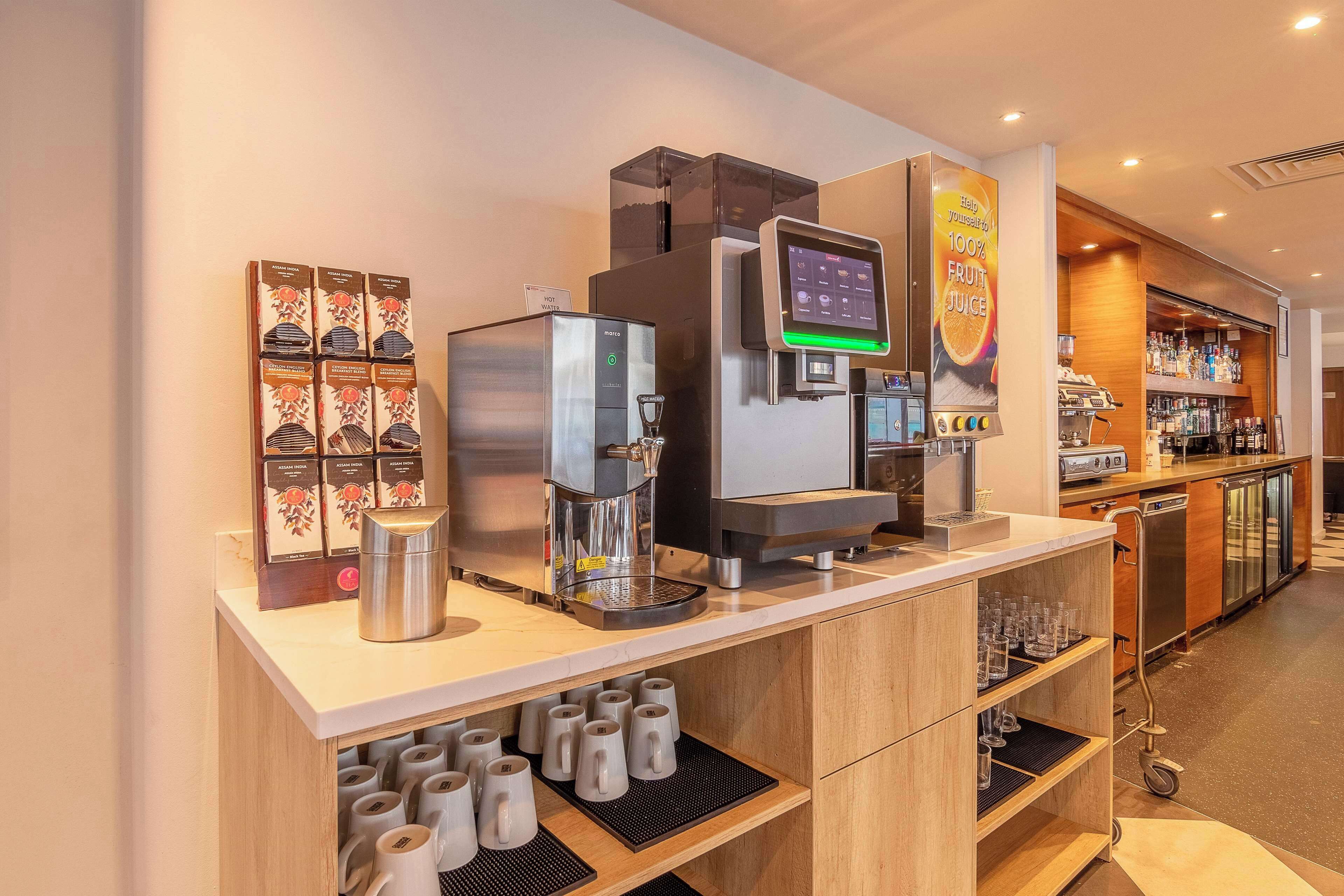 Una cafetería moderna con una máquina de café digital, una selección de cápsulas de café y un escaparate de vidrio.