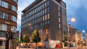 Un hotel moderno con un llamativo letrero 'Encore', que presenta una edificación en esquina con fachada de ladrillo y una estructura rectangular con grandes ventanales.