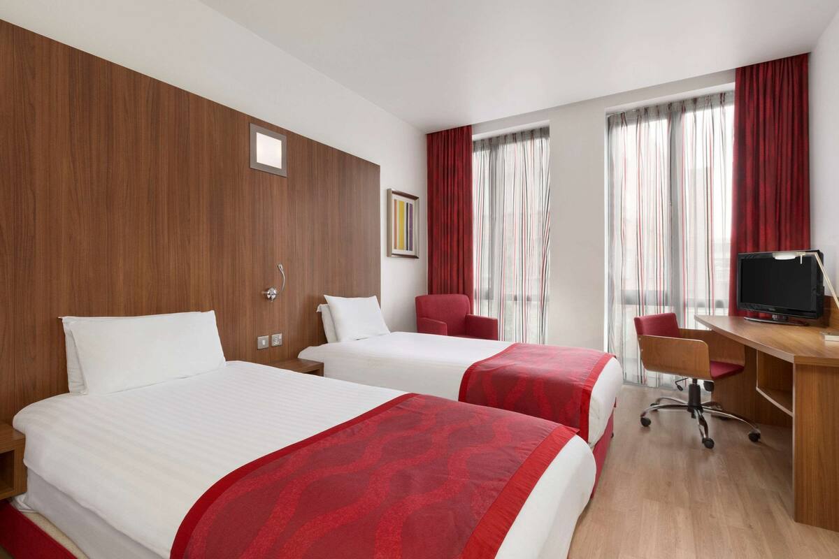 A hotel room with two beds, a desk, a chair, and a TV.
