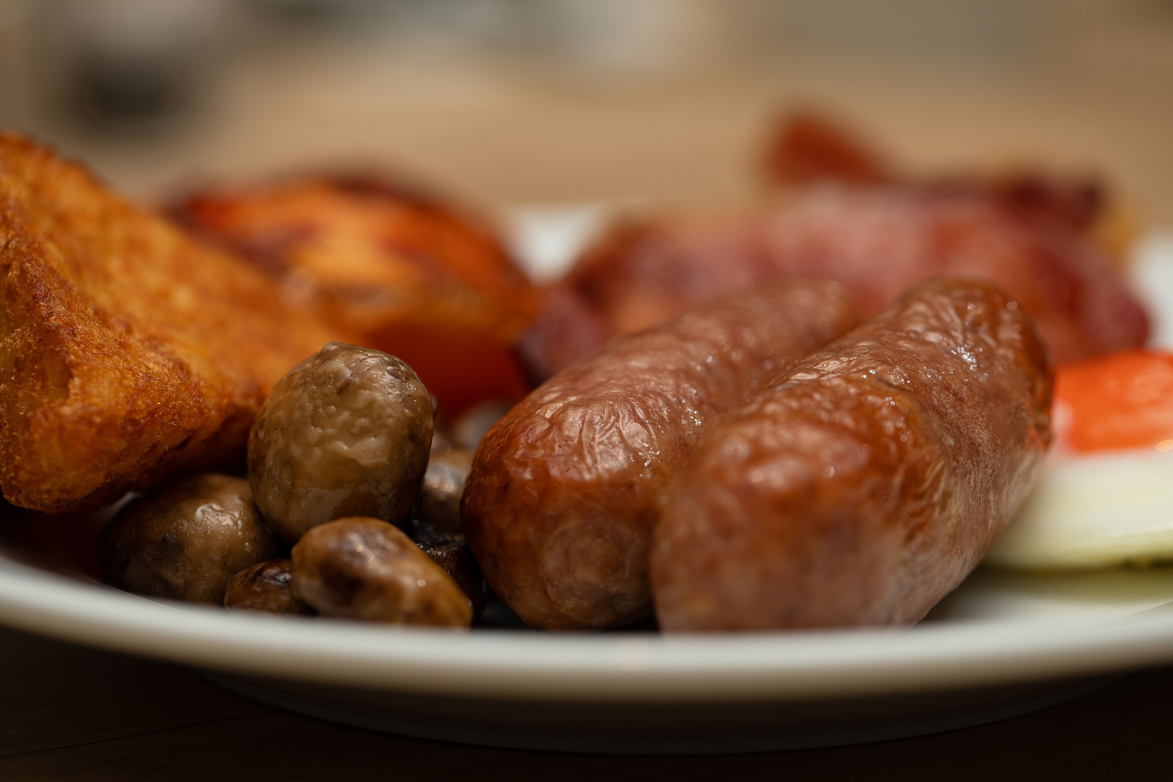 A plate of food including sausages, mushrooms, and a slice of tomato.
