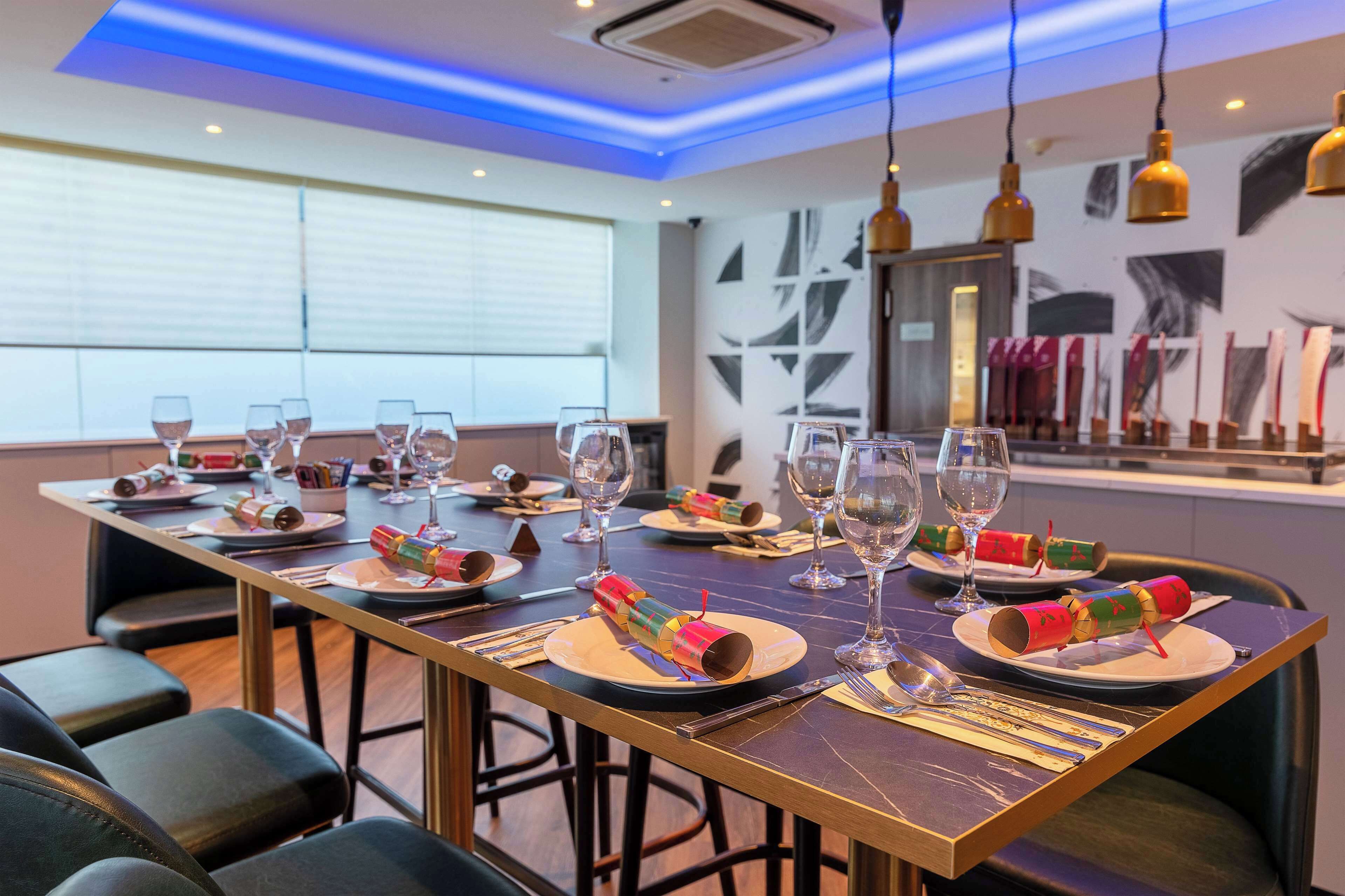 A dining area with a long table set for a meal, featuring colorful paper lanterns, wine glasses, and cutlery.
