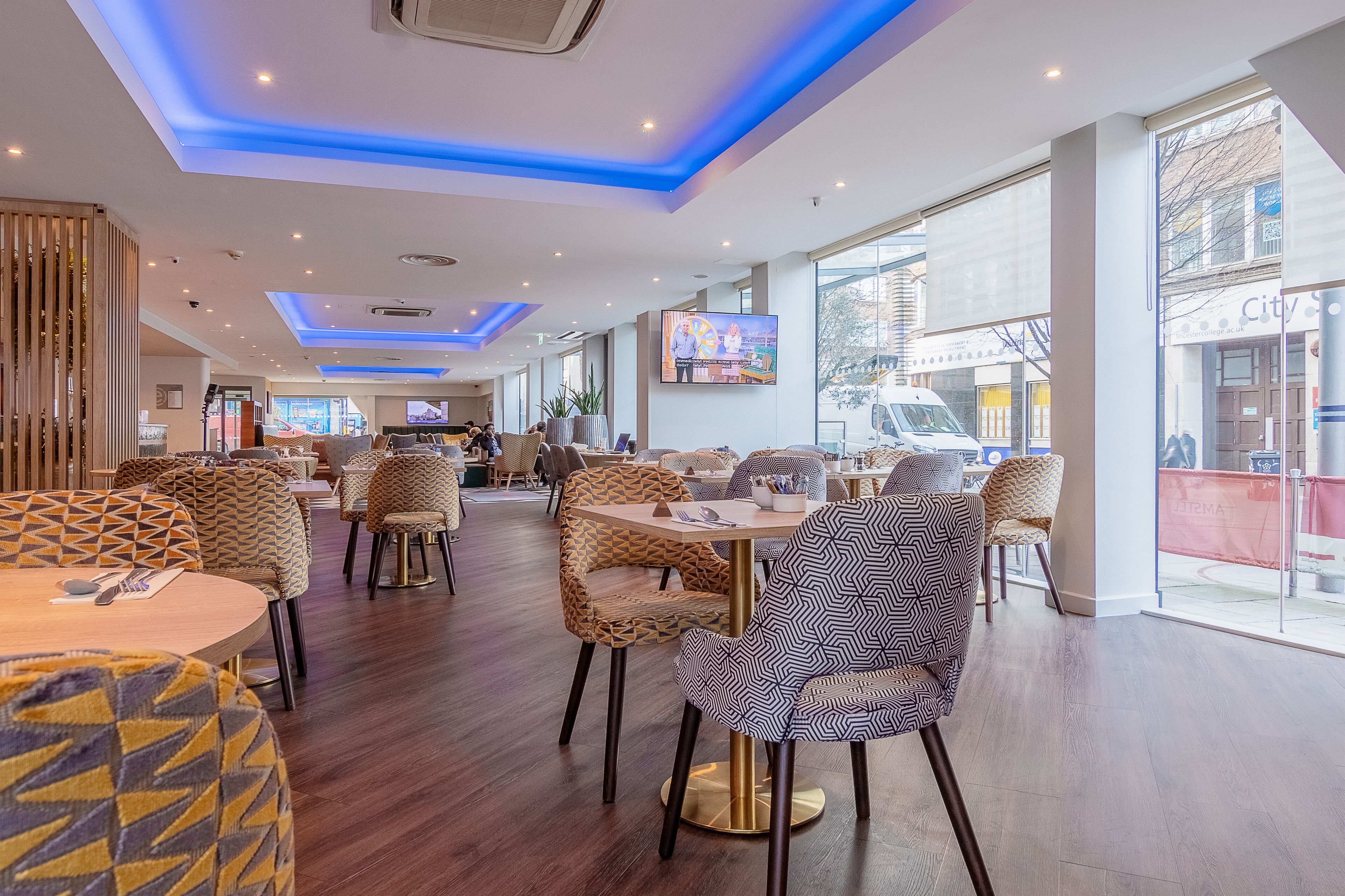 En moderne restaurant med mønstrede stole, runde borde og et stort fjernsyn.