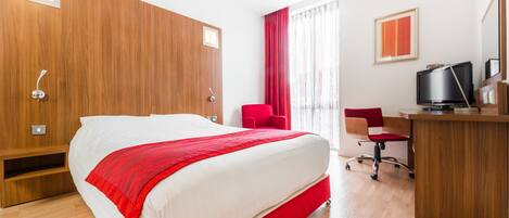 A hotel room with a large bed, a desk, a chair, and a television.
