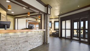 A reception area with a stone wall, wooden counter, and a view of the outside through large glass doors. - Days Inn by Wyndham High Level (High Level)