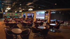 A bar area with multiple tables and chairs, a pool table, and a projection screen displaying a sports event. - Days Inn by Wyndham High Level (High Level)