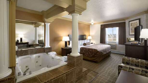 A hotel room with a large bathtub, a bed with a floral bedspread, a desk with a lamp, and a view of the outdoors through the window. - Days Inn by Wyndham High Level (High Level)