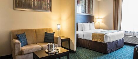 A hotel room with a bed, a sofa, a coffee table, and a painting on the wall.