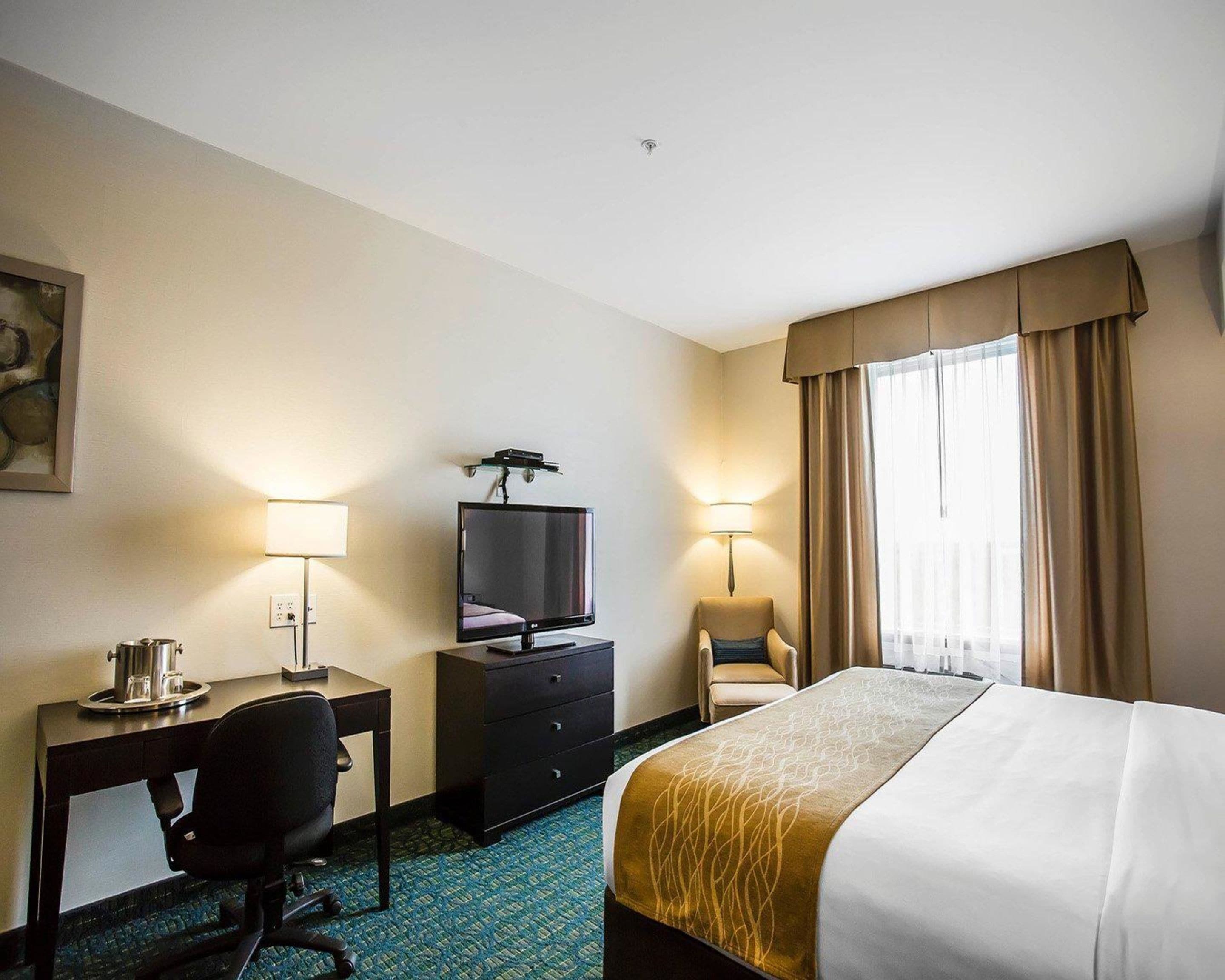A hotel room with a bed, desk, chair, television, and lamps.