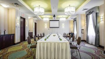 A conference room with a long table, chairs, a projector screen, and chandeliers.