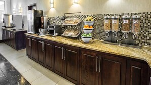 Una cocina de hotel con encimera de mármol, máquina de café, refrigerador y barra de desayuno con diferentes alimentos.