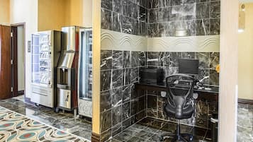 Un espacio de oficina moderno con una pared de mármol, una máquina expendedora, una cafetera y un escritorio con una silla.