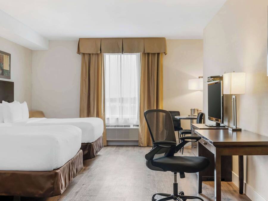 Una habitación de hotel con dos camas, un escritorio con computadora, una silla y un televisor.