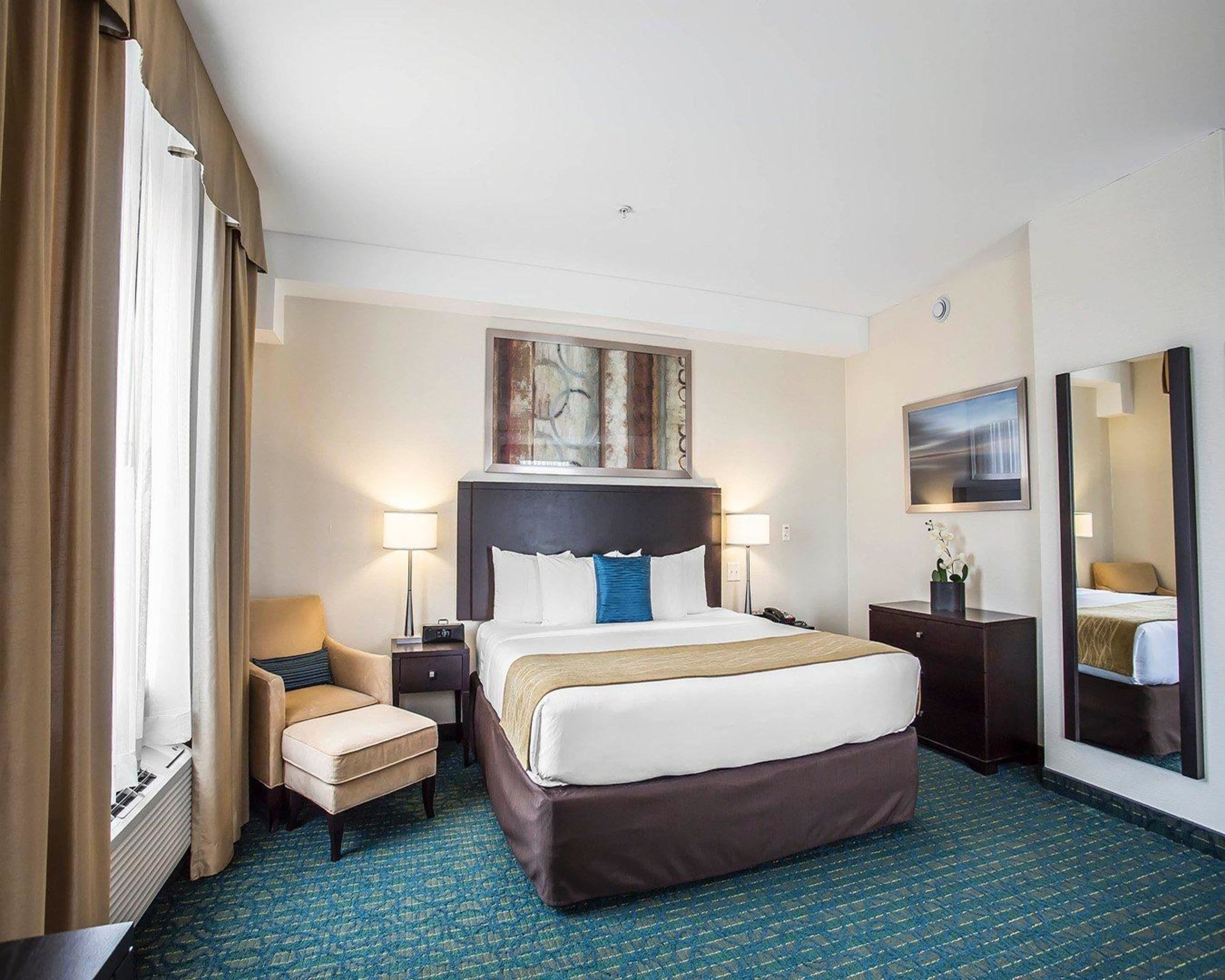 A hotel room with a large bed, two bedside tables, a chair, a desk, a mirror, and artwork on the walls.