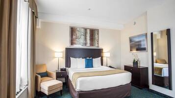 A hotel room with a large bed, two bedside tables, a chair, a desk, a mirror, and artwork on the walls.