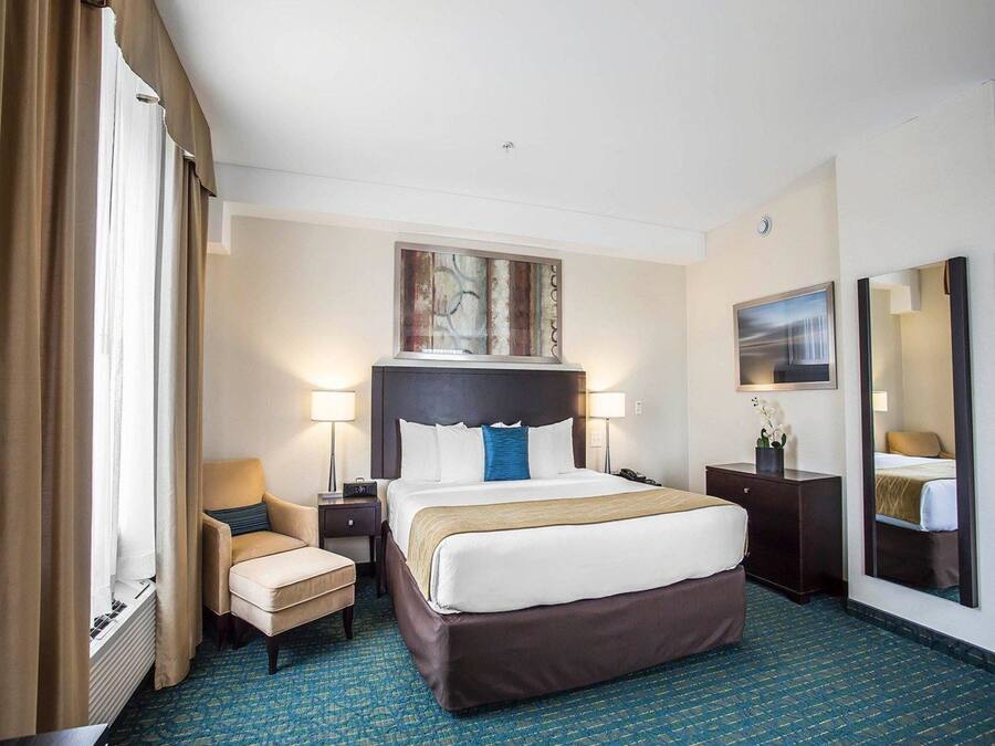 A hotel room with a large bed, two bedside tables, a chair, a desk, a mirror, and artwork on the walls.