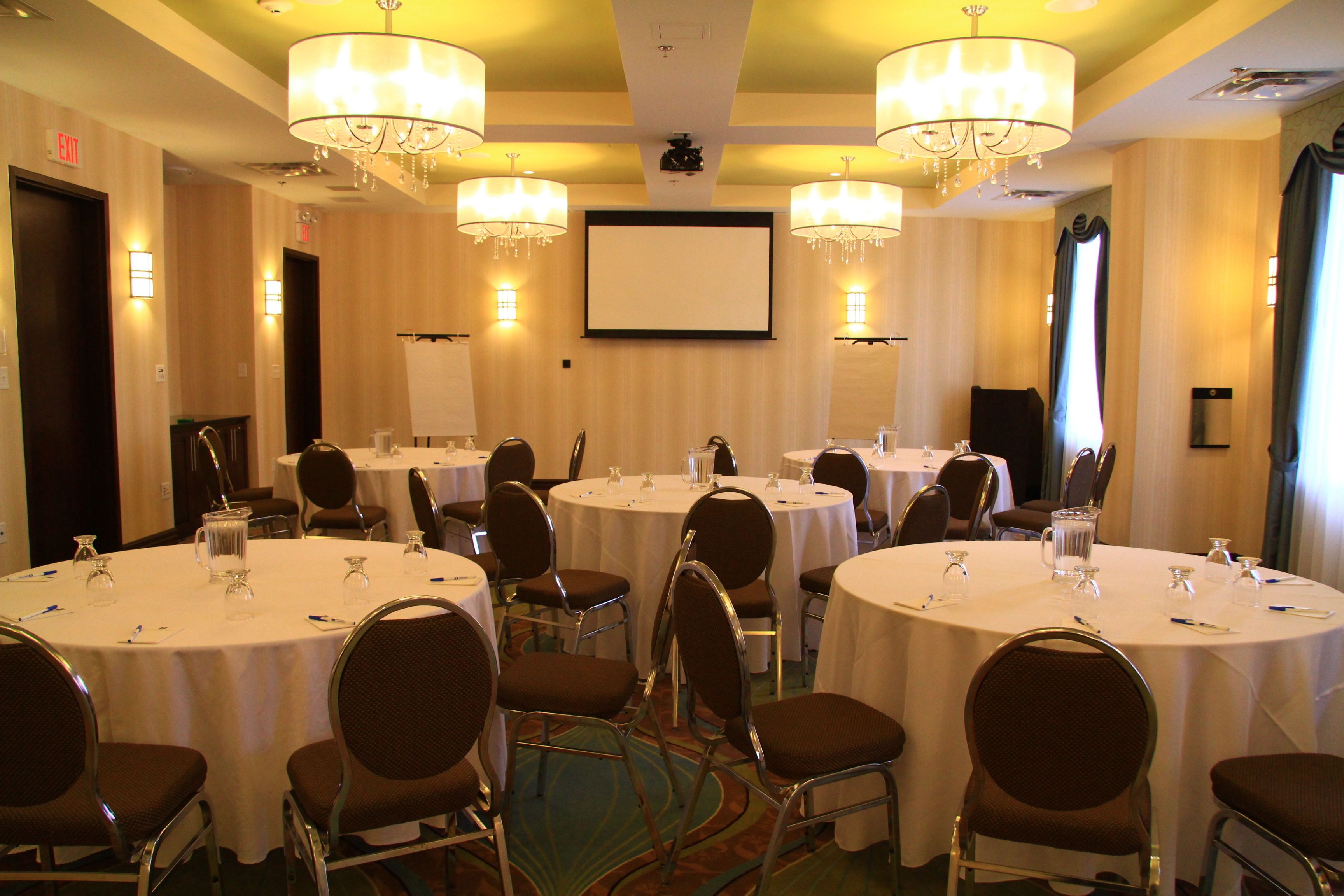 A conference room with multiple round tables, chairs, and chandeliers.