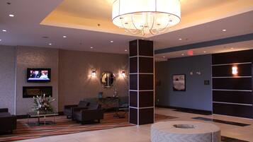 A lobby with a large chandelier, a flat-screen TV, a reception desk, and a seating area with sofas and a coffee table.
