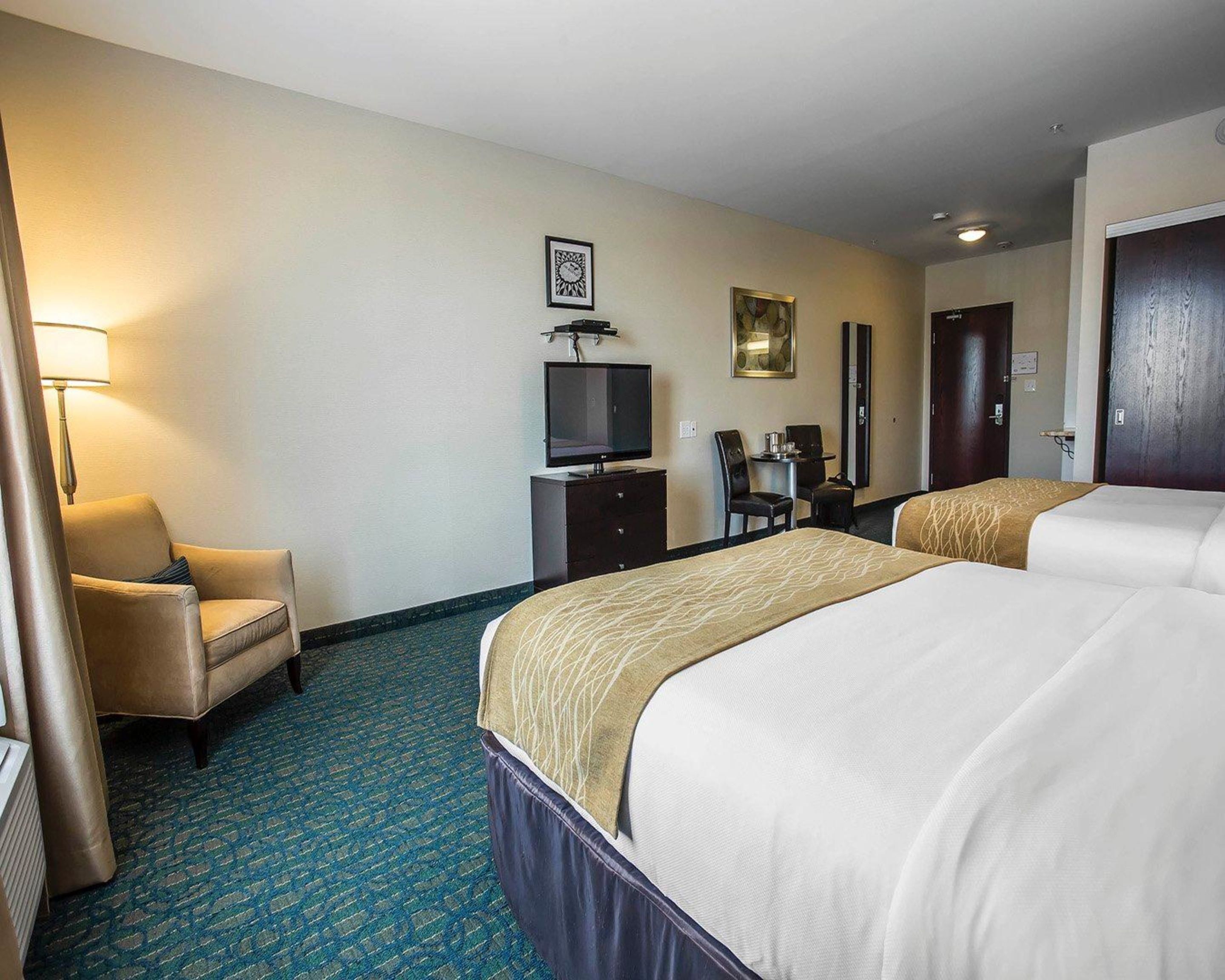 Une chambre d’hôtel avec deux lits, un bureau avec une chaise, une télévision et une lampe.
