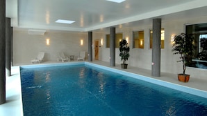 Una piscina interior con agua azul cristalina, rodeada de sillones de descanso y plantas en macetas.