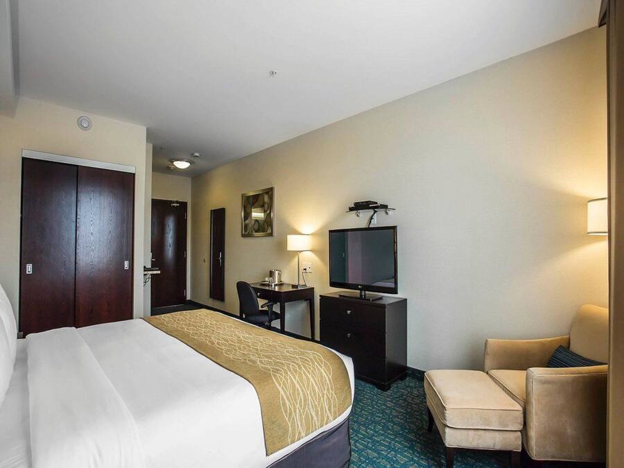 A hotel room with a bed, a desk with a computer, a TV, a chair, and a lamp.