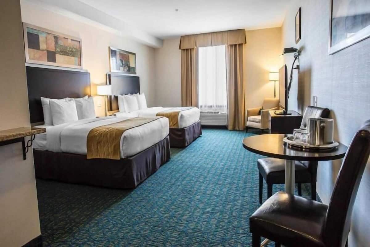 A hotel room with two beds, a desk, a chair, a coffee maker, and a window with curtains.