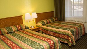 Ein Hotelzimmer mit zwei Betten, jeweils mit einem gemusterten Überwurf, einem Nachttisch mit Lampe und einem Fenster mit Vorhängen.