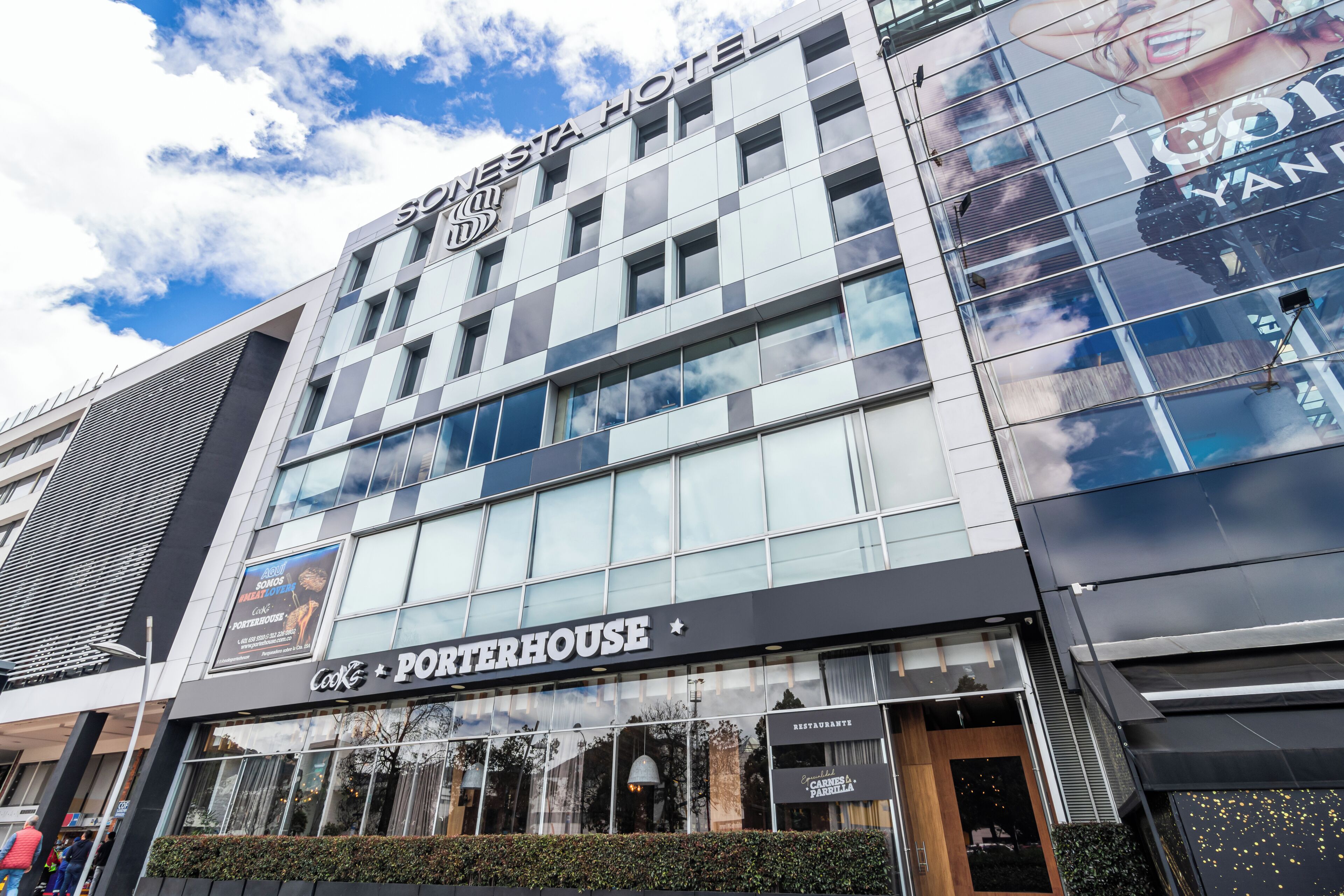 Un hotel con fachada moderna, un restaurante visible llamado Porterhouse y un cielo despejado.