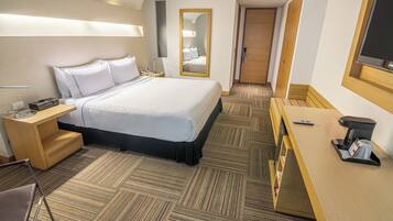 A hotel room with a bed, bedside table, desk, and a mirror.