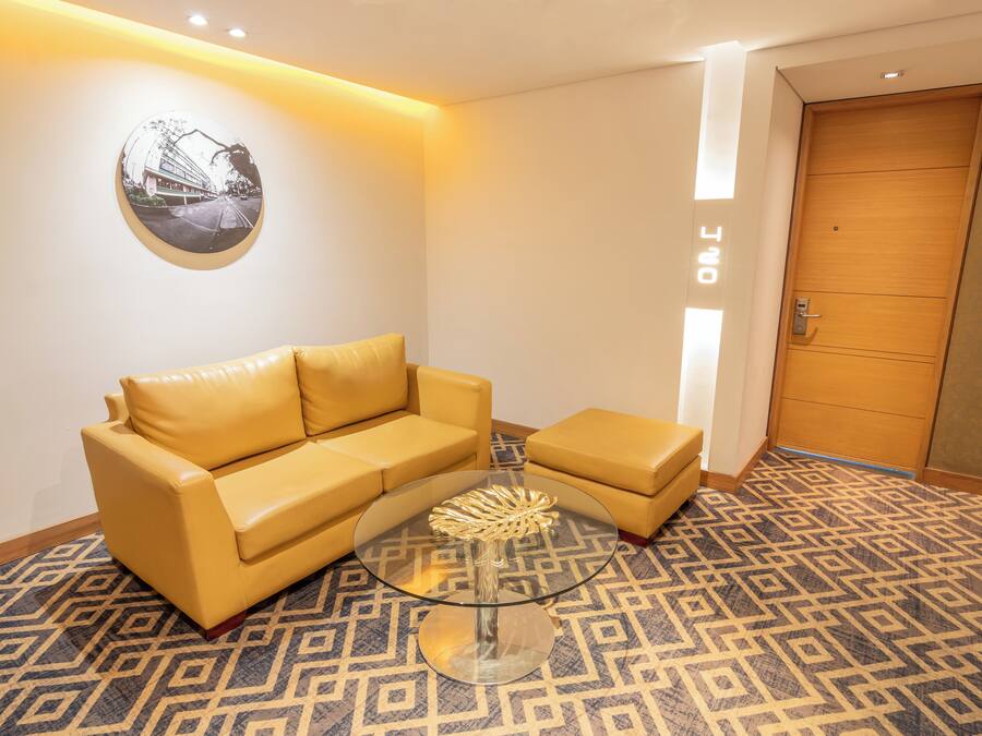 A modern hotel lobby with a yellow leather sofa, a glass coffee table, and a patterned carpet.