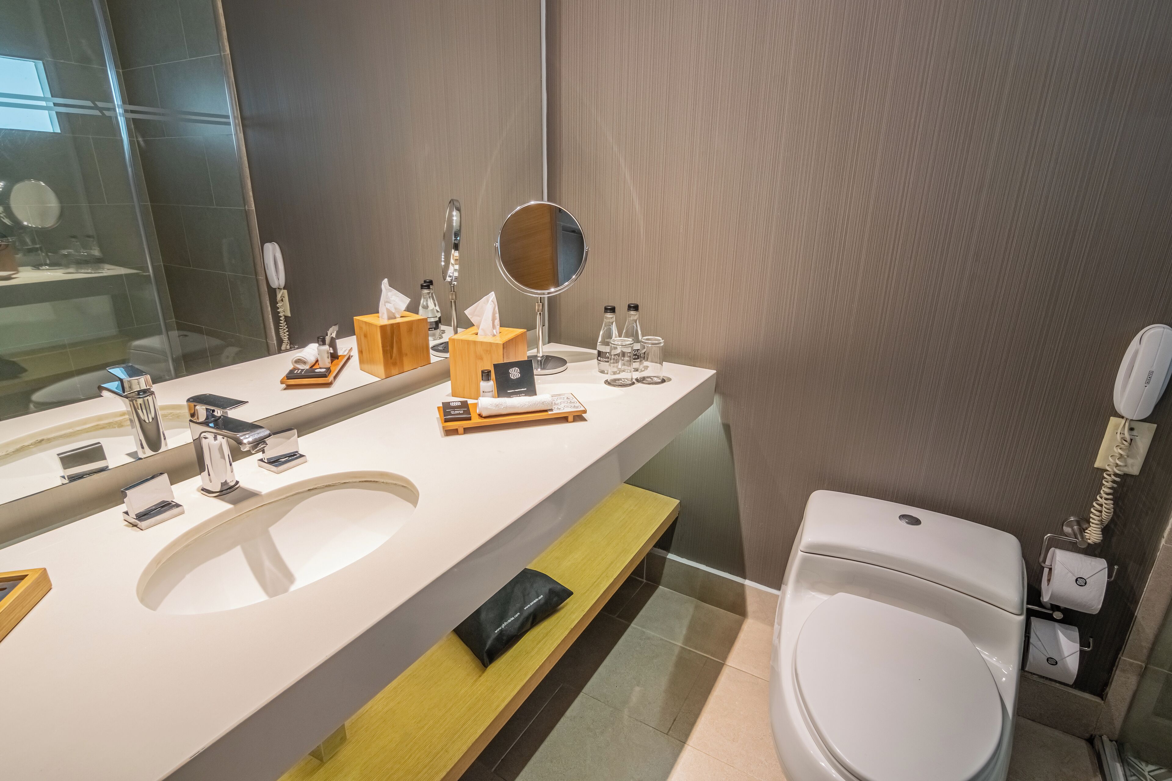 Un baño moderno con un espejo grande, dos lavabos, un inodoro y un banco.