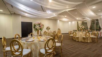 Un salón de banquetes con mesas redondas, sillas doradas y centros de mesa florales.