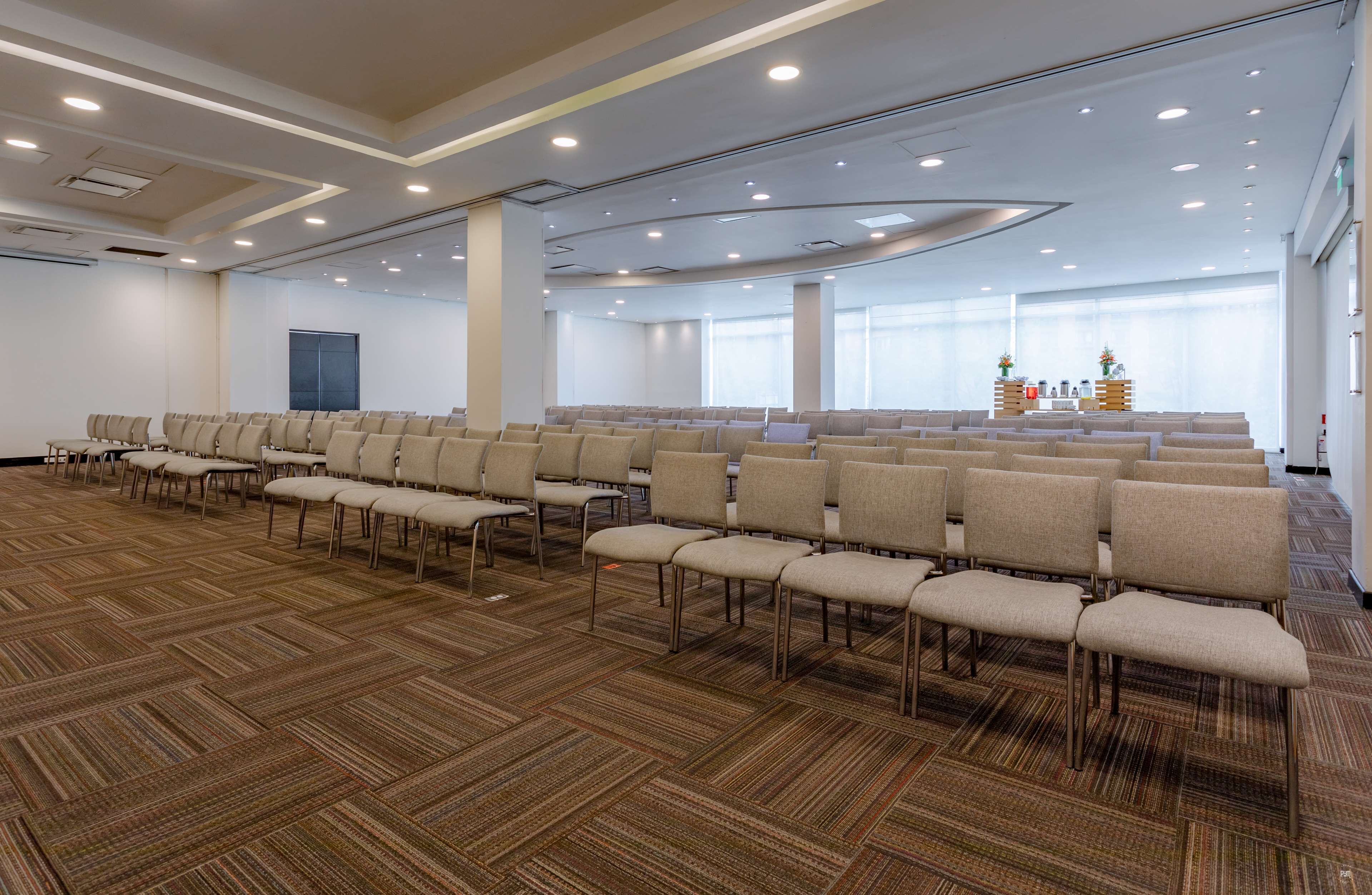 A large conference room with rows of chairs, carpeted flooring, and a stage area with a podium.