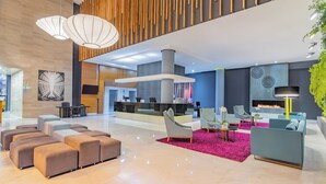 A spacious lobby with a modern design, featuring a seating area with sofas and ottomans, a reception desk, and a fireplace. - Sonesta Hotel Bogota (Bogotá)