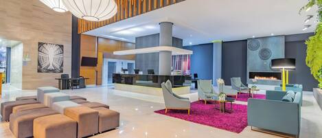 A spacious lobby with a modern design, featuring a seating area with sofas and ottomans, a reception desk, and a fireplace.