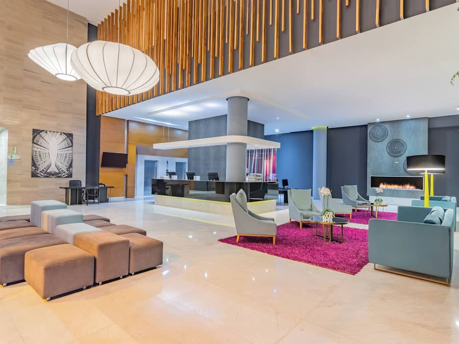 Un lobby espacioso con diseño moderno, que cuenta con una zona de estar con sofás y otomanas, un mostrador de recepción y una chimenea.