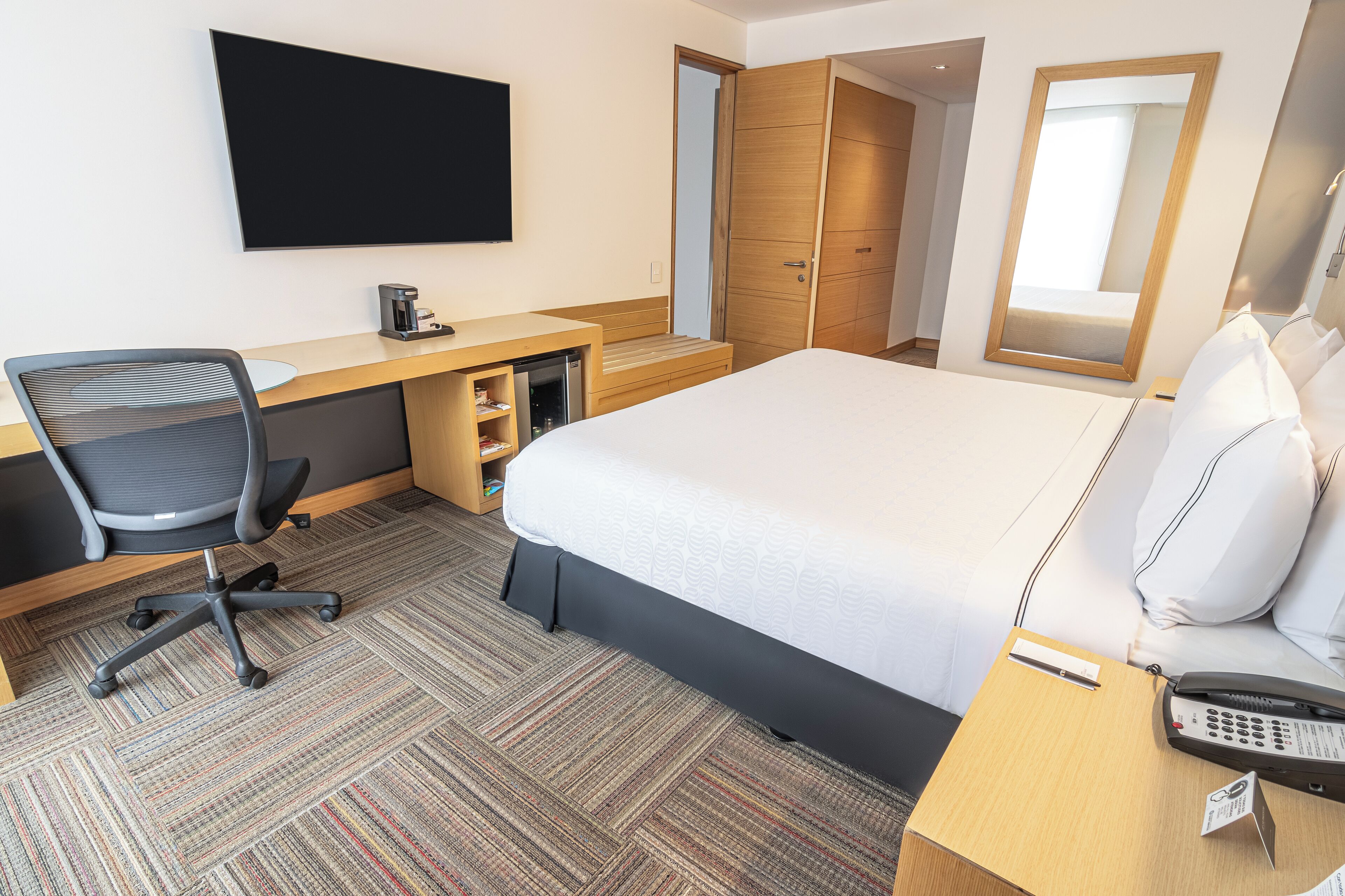 A hotel room with a bed, desk, chair, and a television.