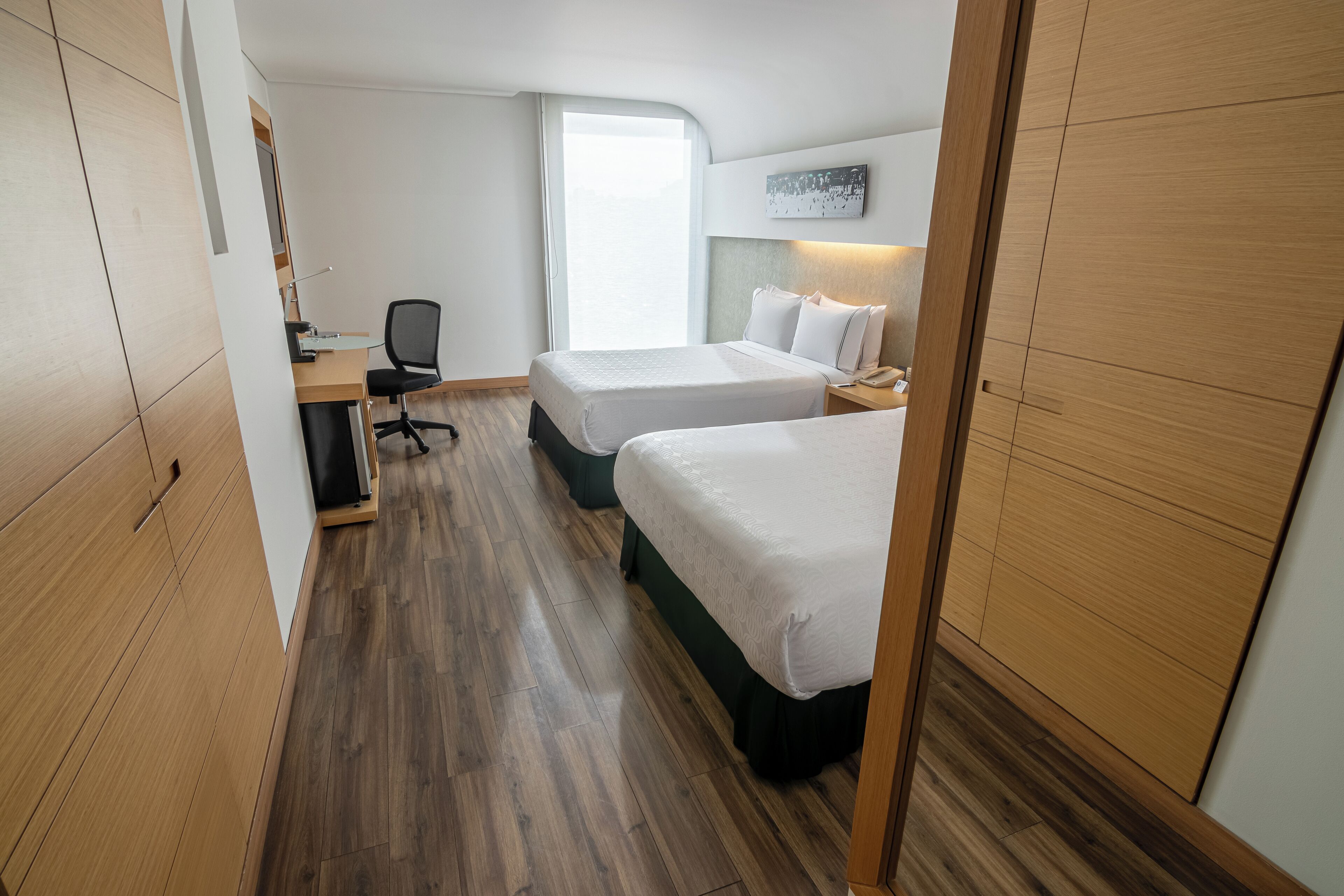 Habitación de hotel con dos camas, un escritorio, una silla, una computadora y una ventana con vistas.