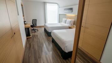 Habitación de hotel con dos camas, un escritorio, una silla, una computadora y una ventana con vistas.