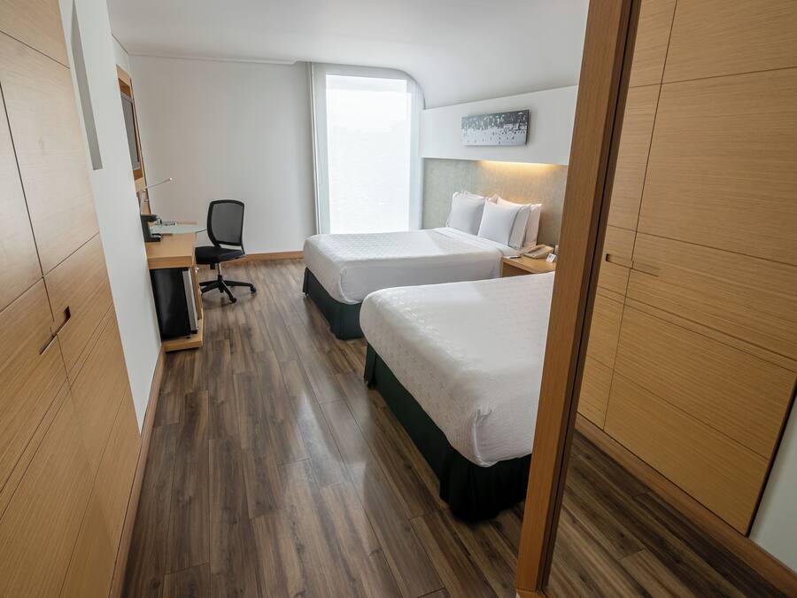 Habitación de hotel con dos camas, un escritorio, una silla, una computadora y una ventana con vistas.