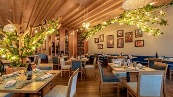 Restaurante com mesas de madeira, cadeiras estofadas em azul e teto de tijolos.