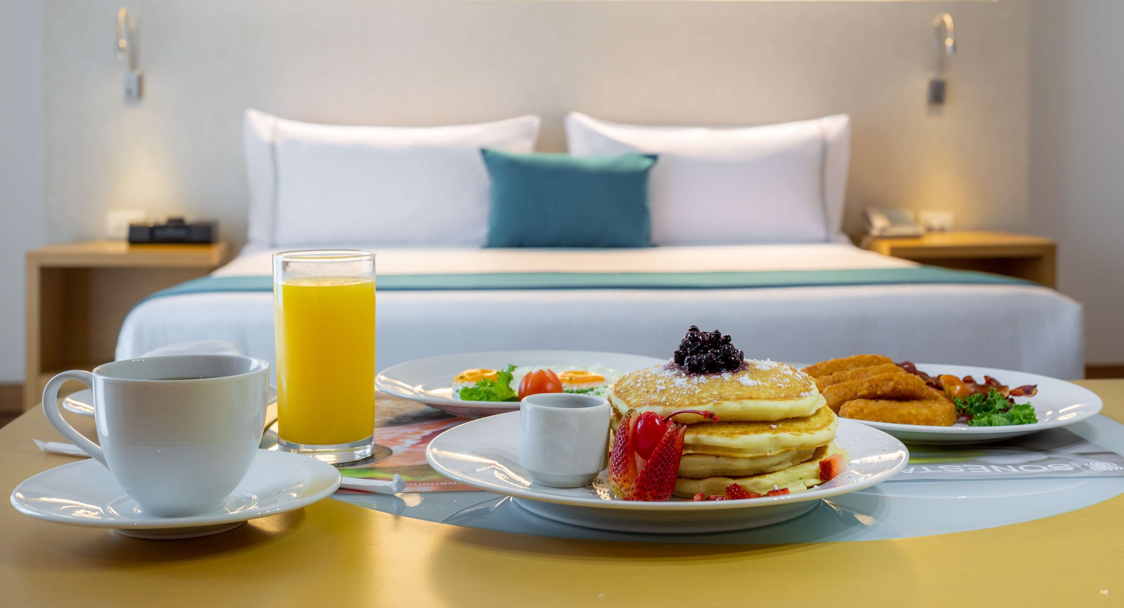Frühstück mit Pfannkuchen, Obst und Croissants auf einem Tisch in einem Hotelzimmer.