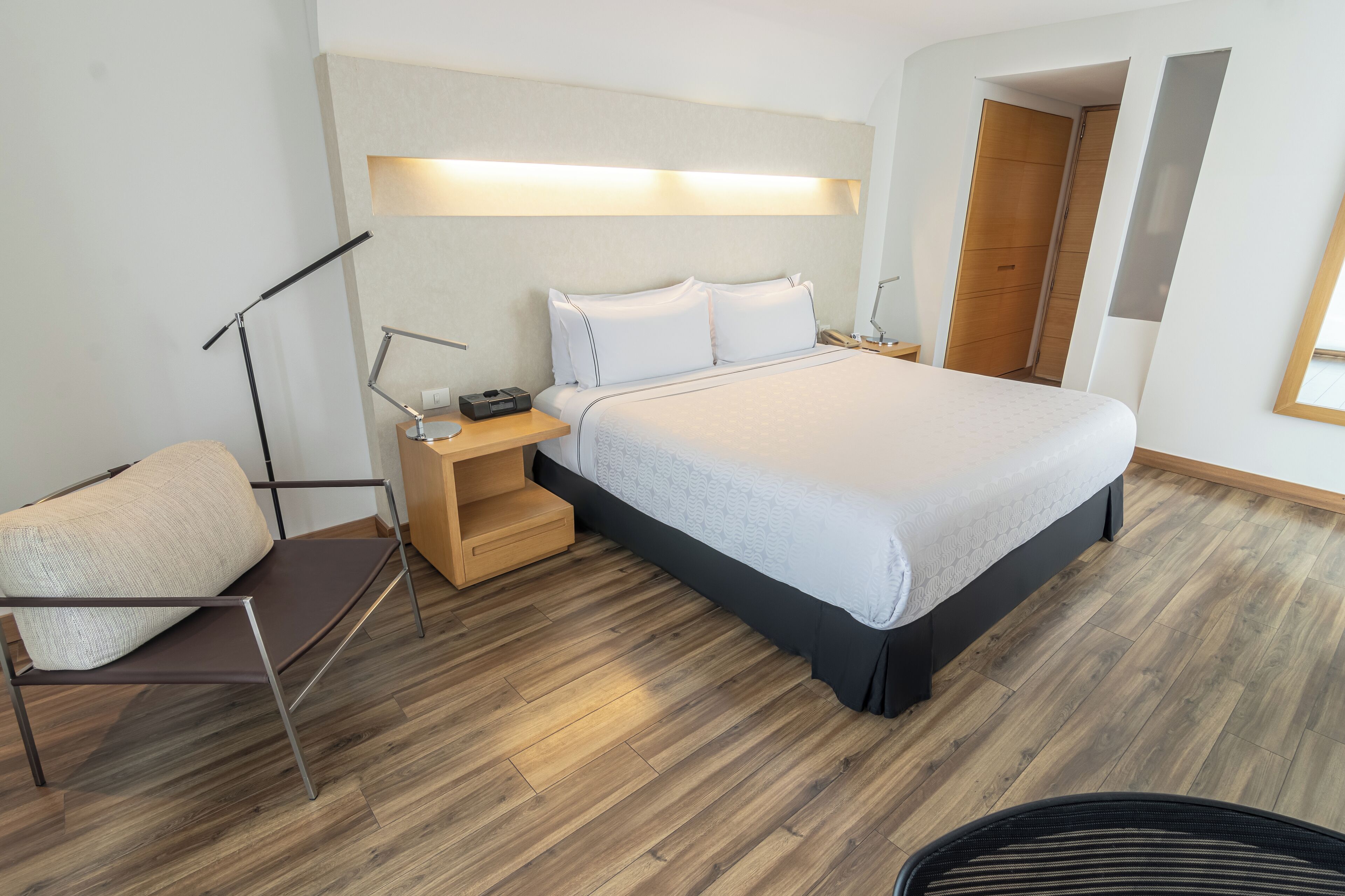 A modern bedroom with a large bed, bedside tables, a reading lamp, and a chair.