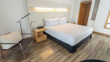 A modern bedroom with a large bed, bedside tables, a reading lamp, and a chair.