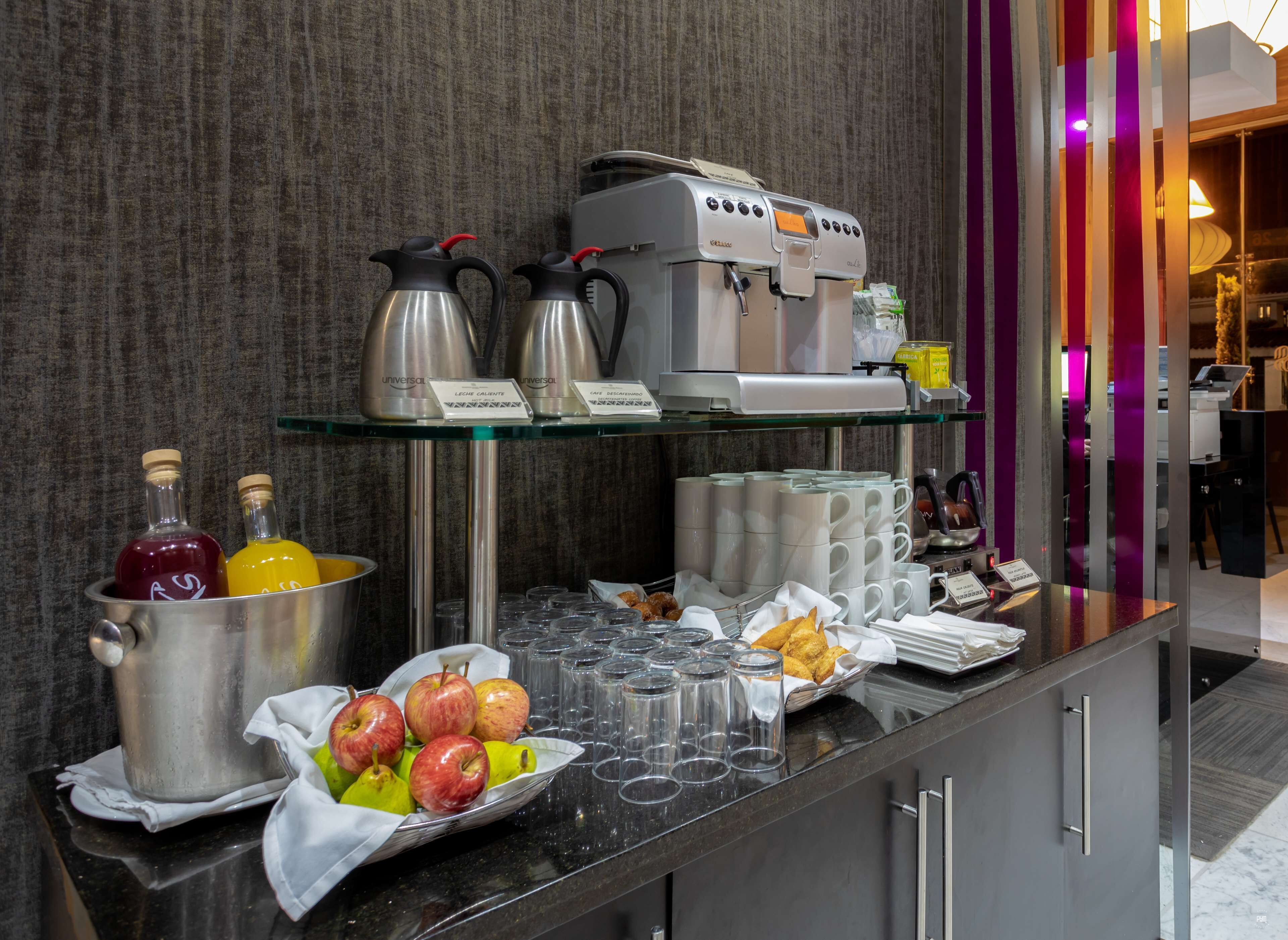 Zona de bufé con máquina de café, jarras de bebidas y frutero.