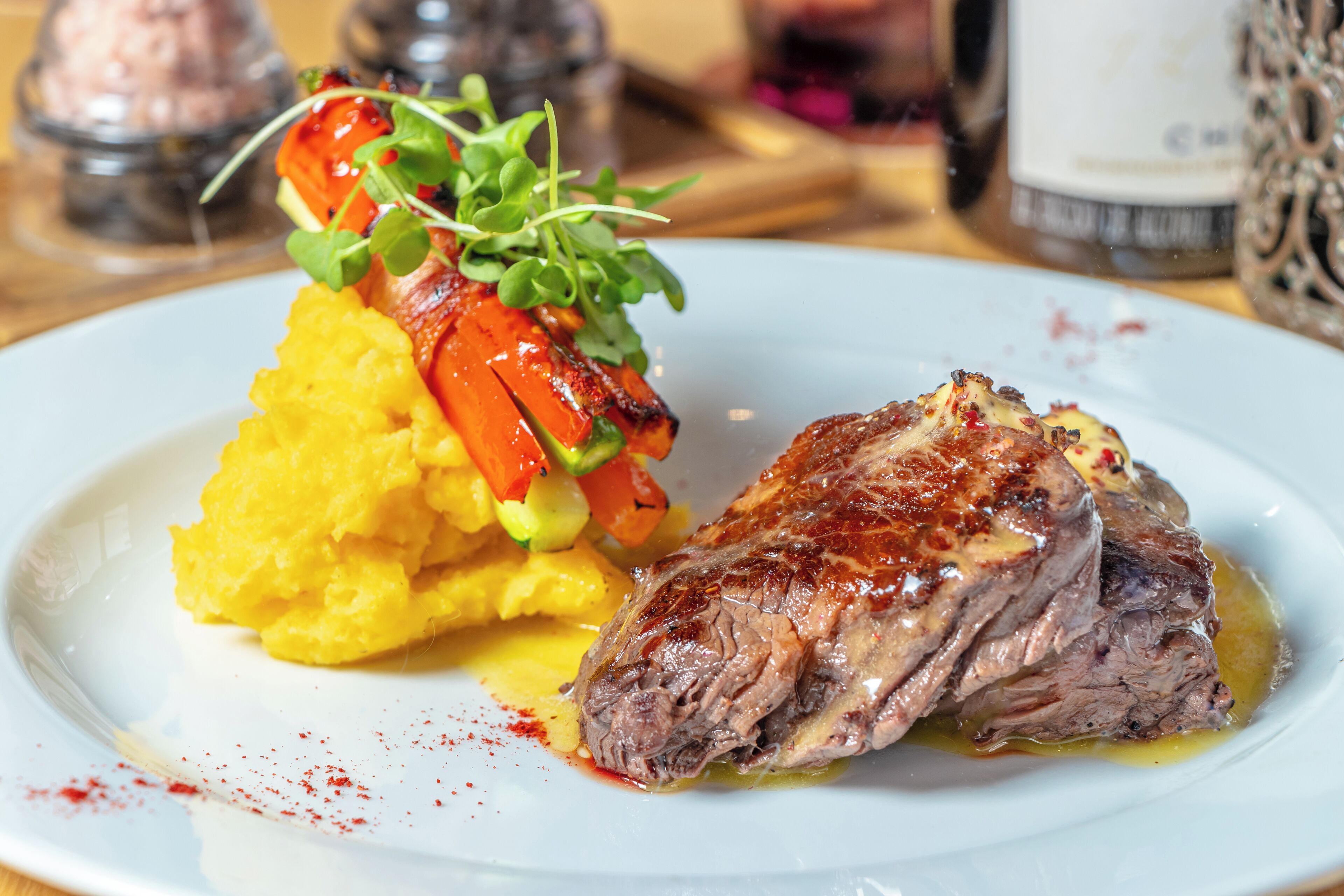 Un plato con un trozo de carne, puré de papas y una guarnición de verdura.