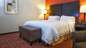 Una habitación de hotel con cama, mesita de noche, lámpara, banco y alfombra estampada.