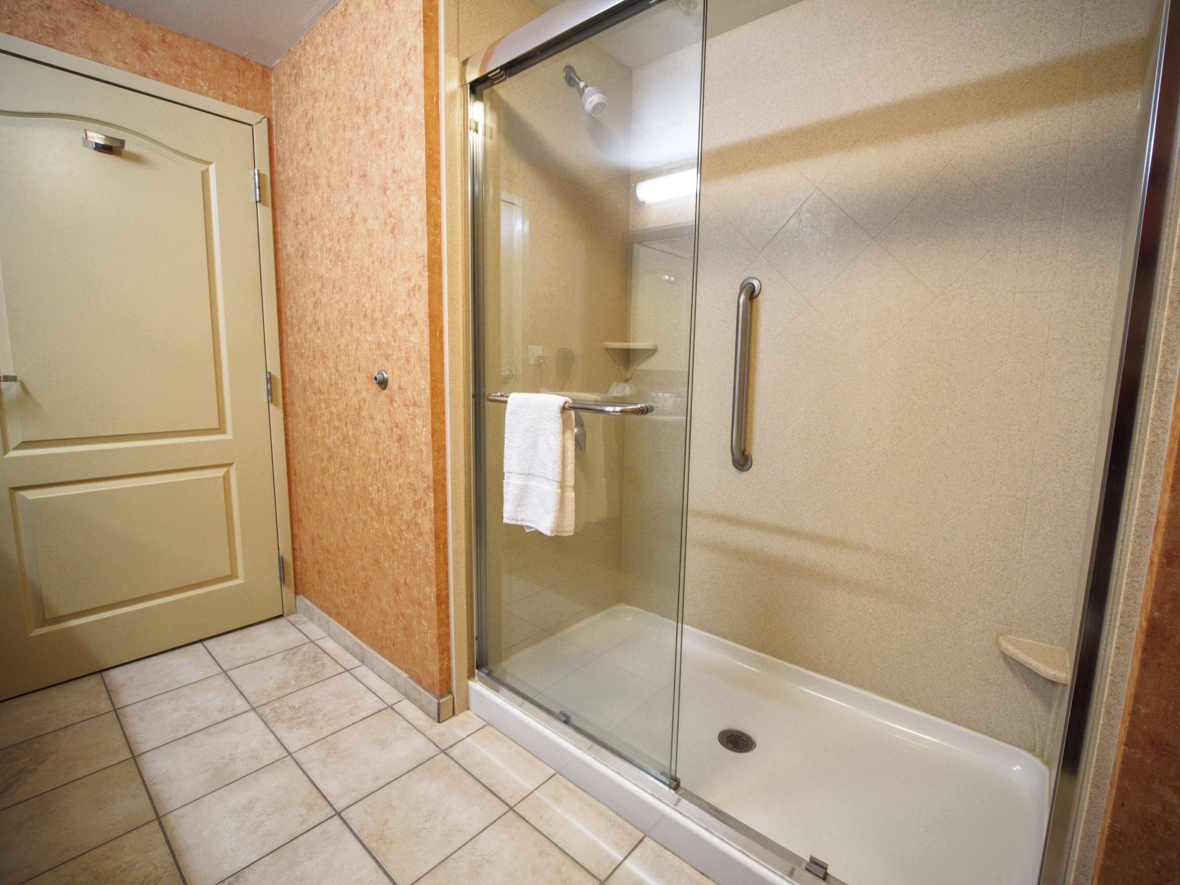 A bathroom with a glass-enclosed shower, a white towel hanging on the door, and a tiled floor.