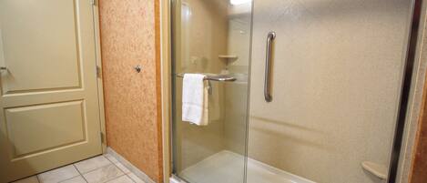 Un baño con cabina de ducha de vidrio, una toalla blanca colgada en la puerta y suelo de baldosas.