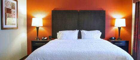 A hotel room with a large bed, two bedside tables with lamps, a framed picture on the wall, and an orange accent wall.
