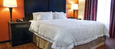 Habitación de hotel con una cama grande, dos mesitas de noche con lámparas, cabecero y alfombra estampada.